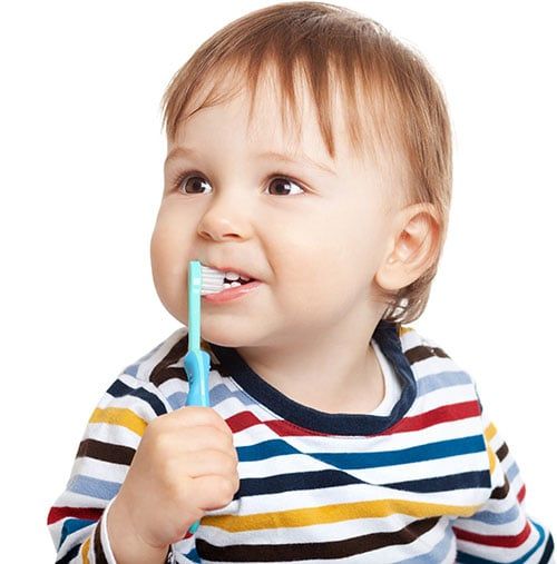 toddler holding a toothbrush against his mouth exposing his teeth